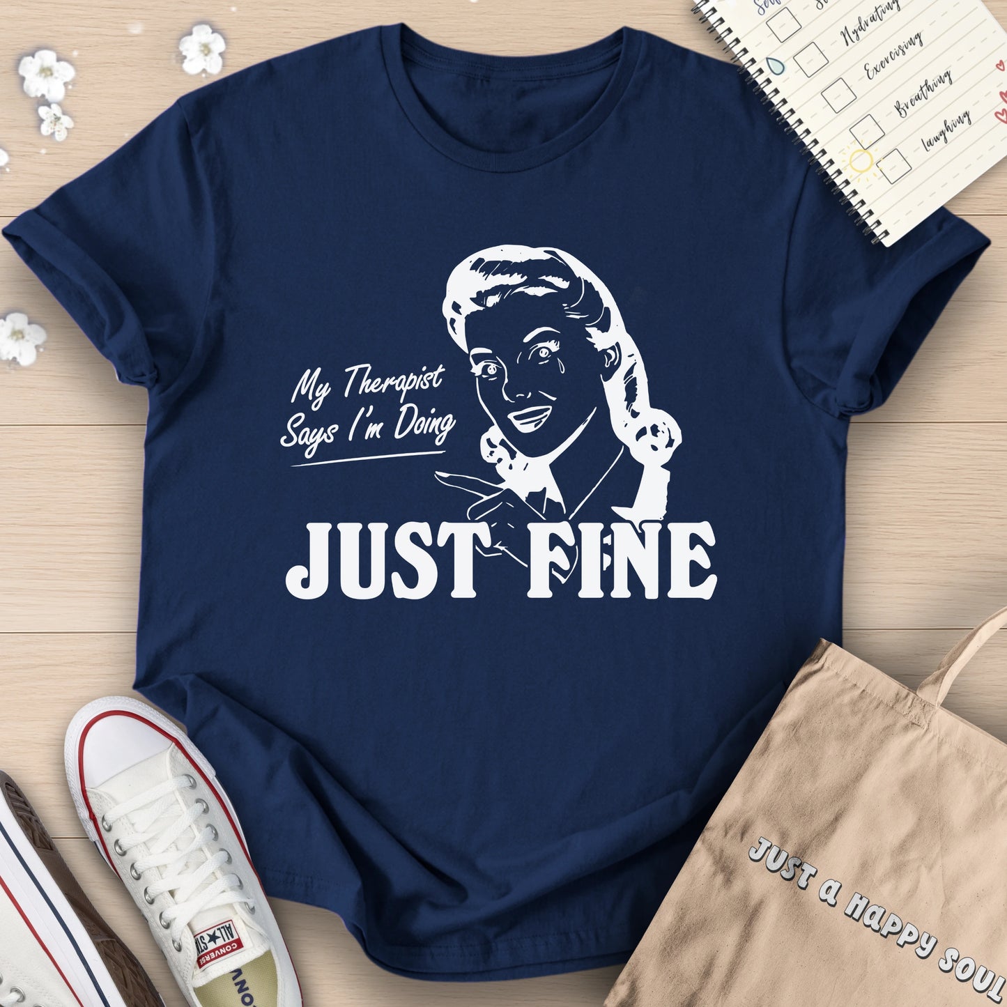 Navy blue t-shirt with graphic and text 'My Therapist Says I'm Doing Just Fine' on a wooden surface.